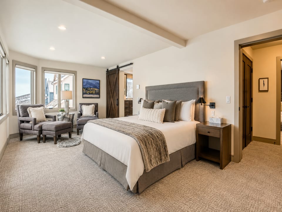 Sink into the plush king bed after a day exploring, with sunlight streaming through large windows. Your peaceful retreat features a cozy seating nook and rustic barn door charm.