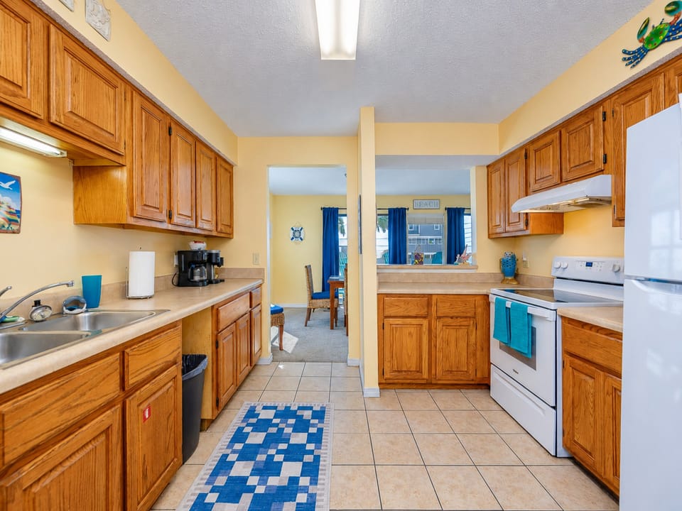 This kitchen features warm wood cabinetry, a double sink, and a view into the dining area with natural light streaming in