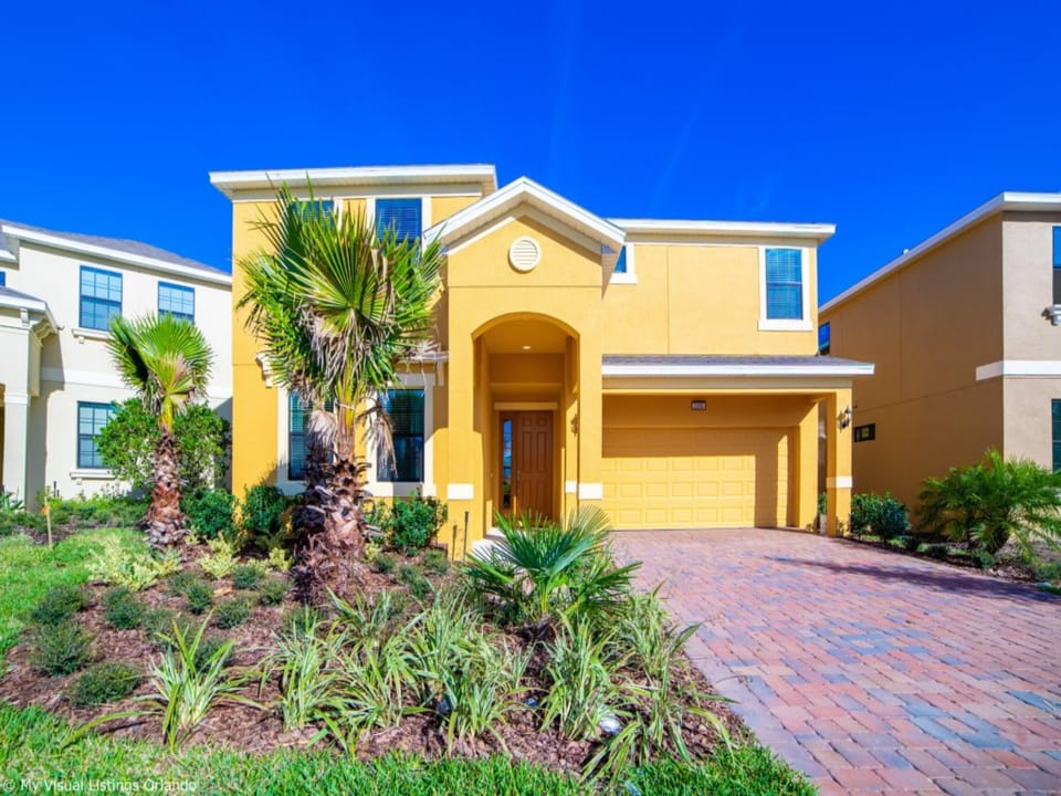 Charming yellow villa with lush landscaping and a welcoming driveway.