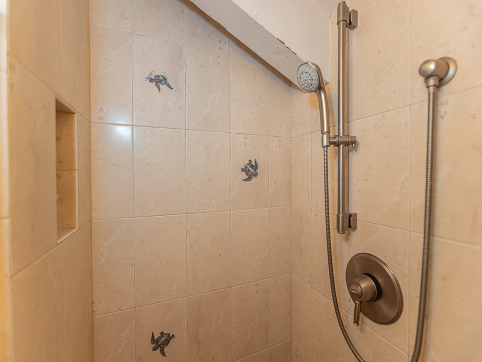 Step into your private shower featuring warm tile, a handheld showerhead, and elegant turtle tile accents—perfect for refreshing after a day of adventure.