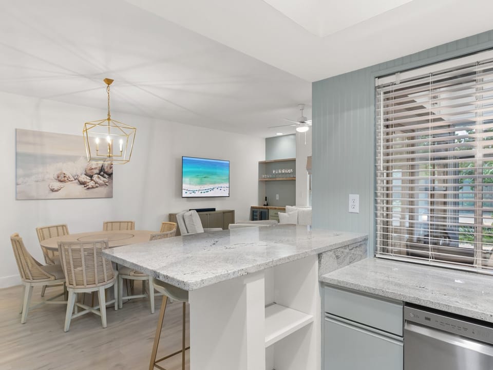 This airy coastal kitchen opens to a bright dining and living area, creating a seamless flow for entertaining. Featuring granite countertops, beachy tones, and modern finishes, the space blends style and function with a relaxed seaside vibe.