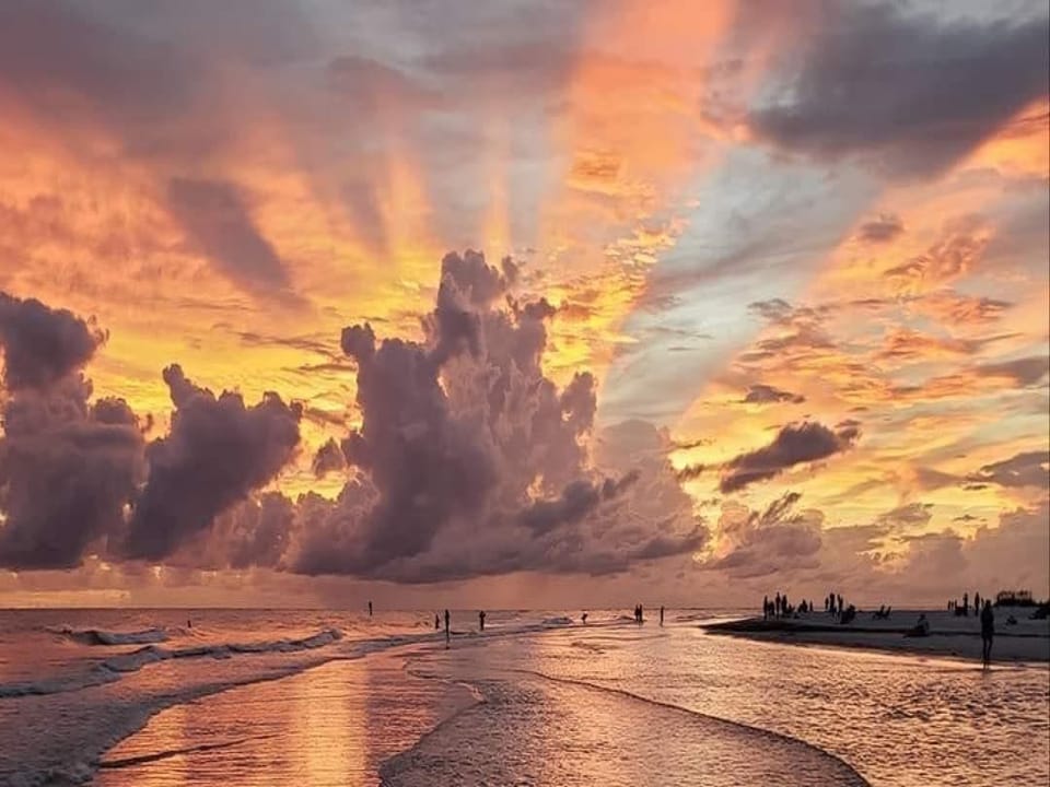 A stunning beachfront sunset paints the sky in brilliant oranges and golds, with gentle waves rolling onto the sand as the day comes to a peaceful close.