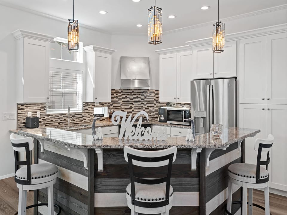 Elegant coastal kitchen with granite countertops, stainless steel appliances, and a shiplap island accented by pendant lighting—inviting guests to gather, cook, and enjoy time together.