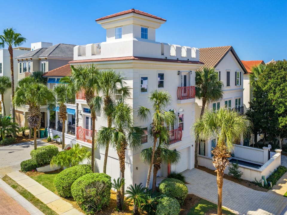Elegant Mediterranean-style beach home in Destin with palm-lined landscaping, balconies, and rooftop views—just steps from the Gulf’s sugar-white sands and emerald waters.