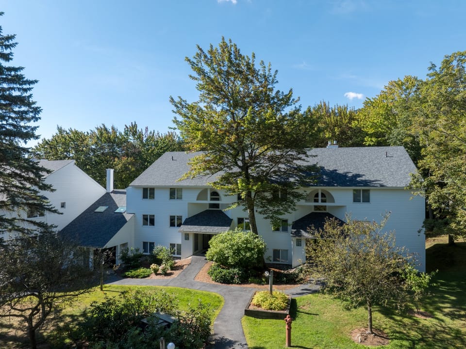 Aerial view shows the property nestled among mature trees in a peaceful residential neighborhood with well-maintained landscaping.