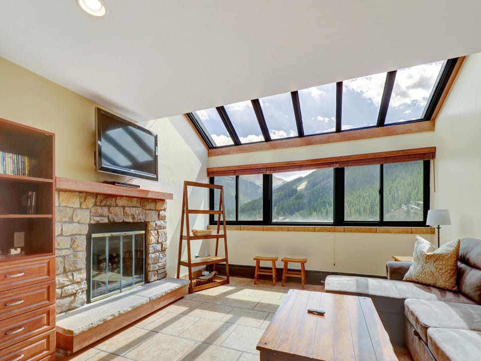 Stunning living space with a full-length skylight and wide windows framing panoramic views of Copper Mountain. Features a stone fireplace and wall-mounted TV for cozy après-ski evenings.