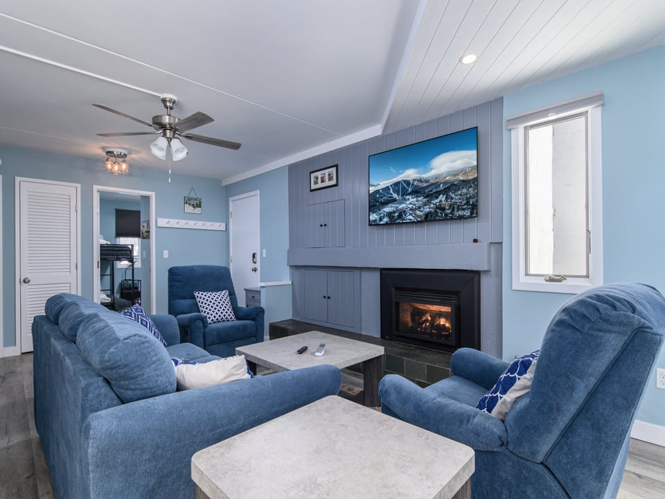 Relax in your cozy living room featuring plush blue seating, a warm fireplace, and modern entertainment setup perfect for unwinding after your adventures.