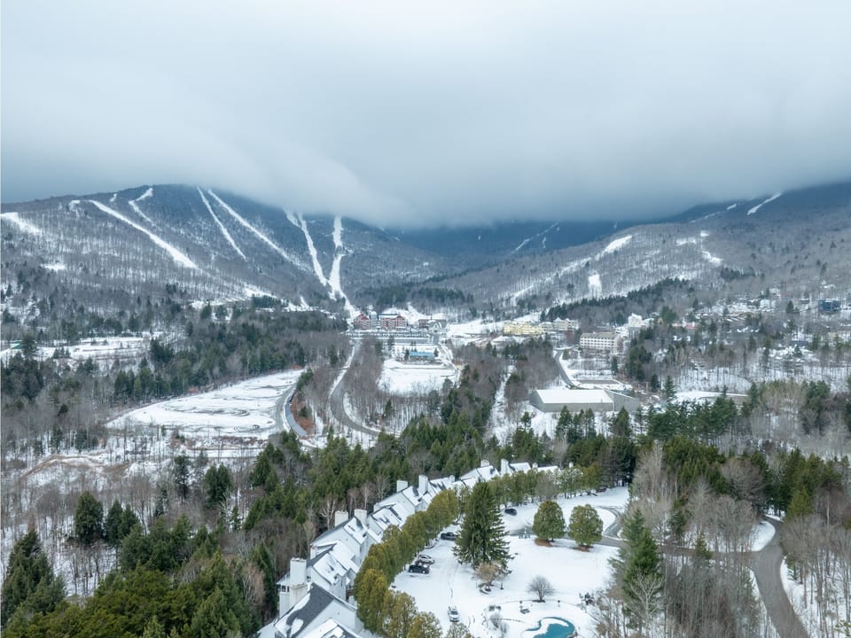 Aerial winter view of the mountainous ski resort area with snow-covered slopes and surrounding forest landscape.