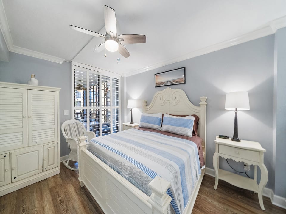 Drift off to sleep in this serene bedroom featuring a plush bed with coastal-inspired linens, gentle ceiling fan, and your own private balcony access for morning coffee or evening relaxation.