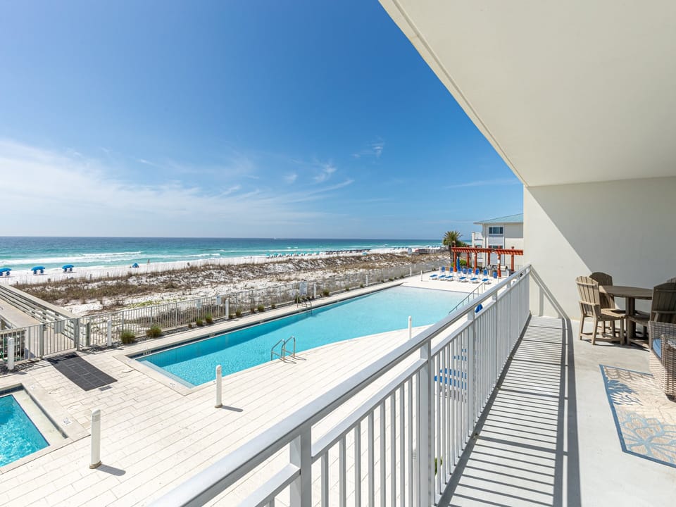 Stunning beachfront balcony with panoramic ocean views, pool access, and outdoor seating overlooking pristine sandy shores.
