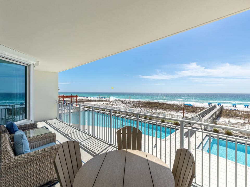 Relax on your private balcony with stunning ocean views, poolside dining table, and comfortable seating overlooking pristine beach.