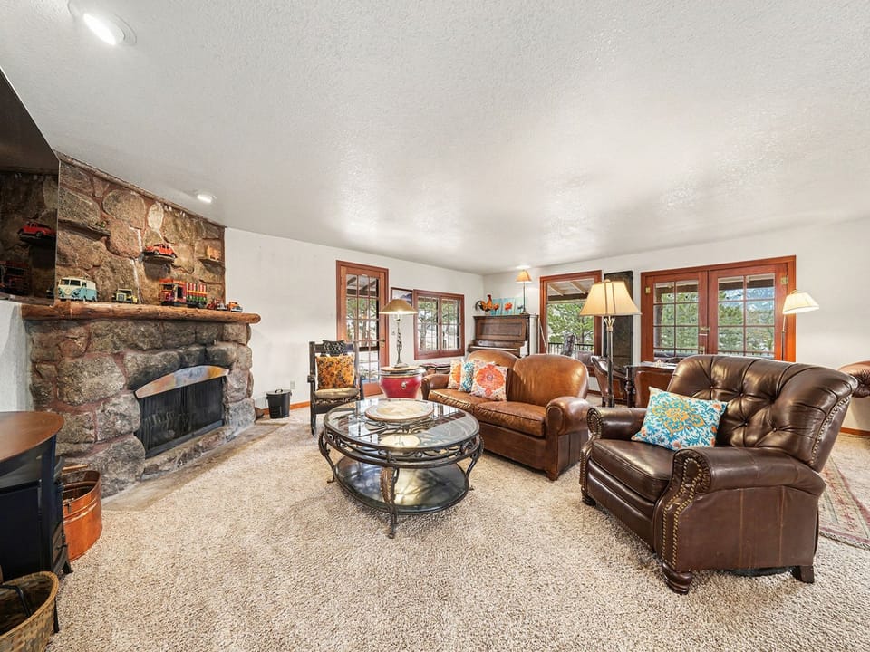 Unwind in your cozy living room with plush leather sofas, crackling stone fireplace, and warm wood accents creating the perfect mountain retreat atmosphere.