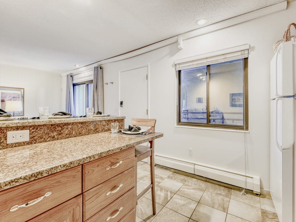 A functional kitchen with granite countertops, wooden cabinetry, and modern appliances, bathed in natural light from large windows overlooking the surrounding area.