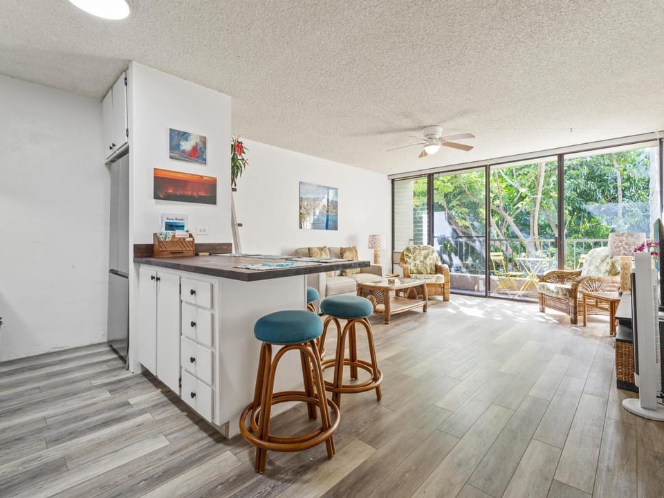 Step into this sun-filled coastal retreat where island-style furnishings meet modern comfort. Natural light streams through sliding glass doors framing lush tropical greenery, while a breakfast bar invites morning coffee and oceanside living.