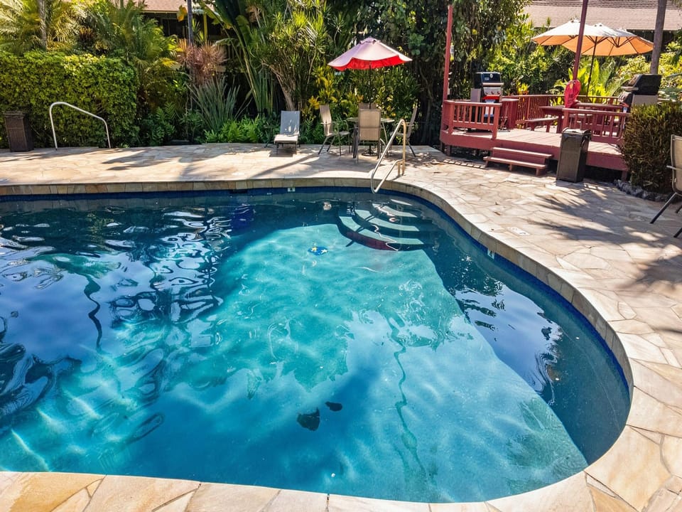 A sparkling pool awaits surrounded by lush tropical greenery, sun loungers, shaded seating, and BBQ facilities for your perfect outdoor escape.