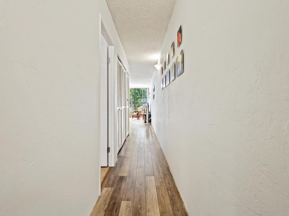 Step into this bright hallway with warm wood floors guiding you toward inviting living spaces and a lush outdoor patio visible ahead.