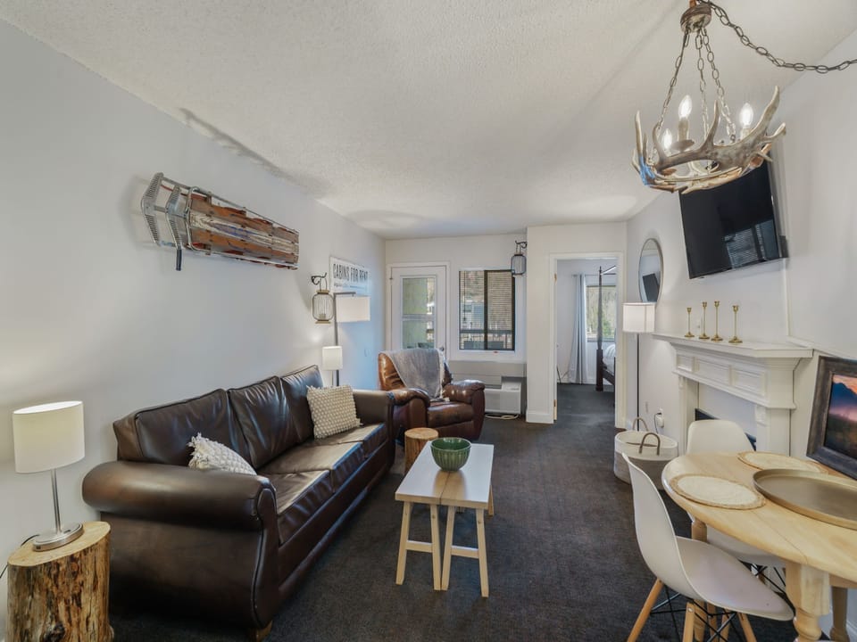 Unwind in your stylish living space with leather seating, antler chandelier, and cozy fireplace creating the perfect mountain retreat atmosphere.