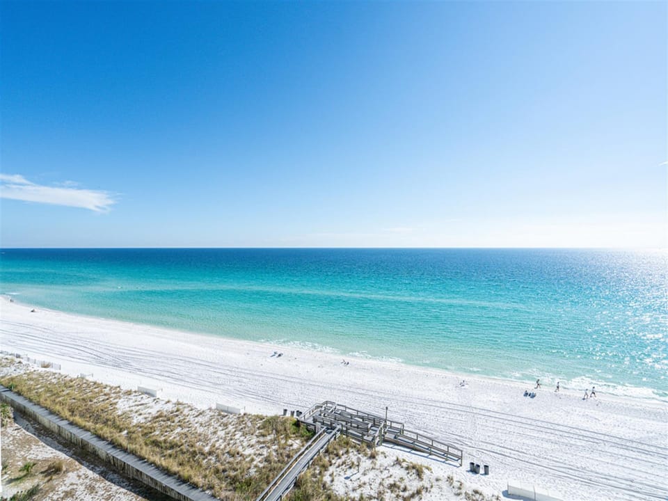 Pristine white sand beach stretches alongside crystal-clear turquoise waters under brilliant blue skies.