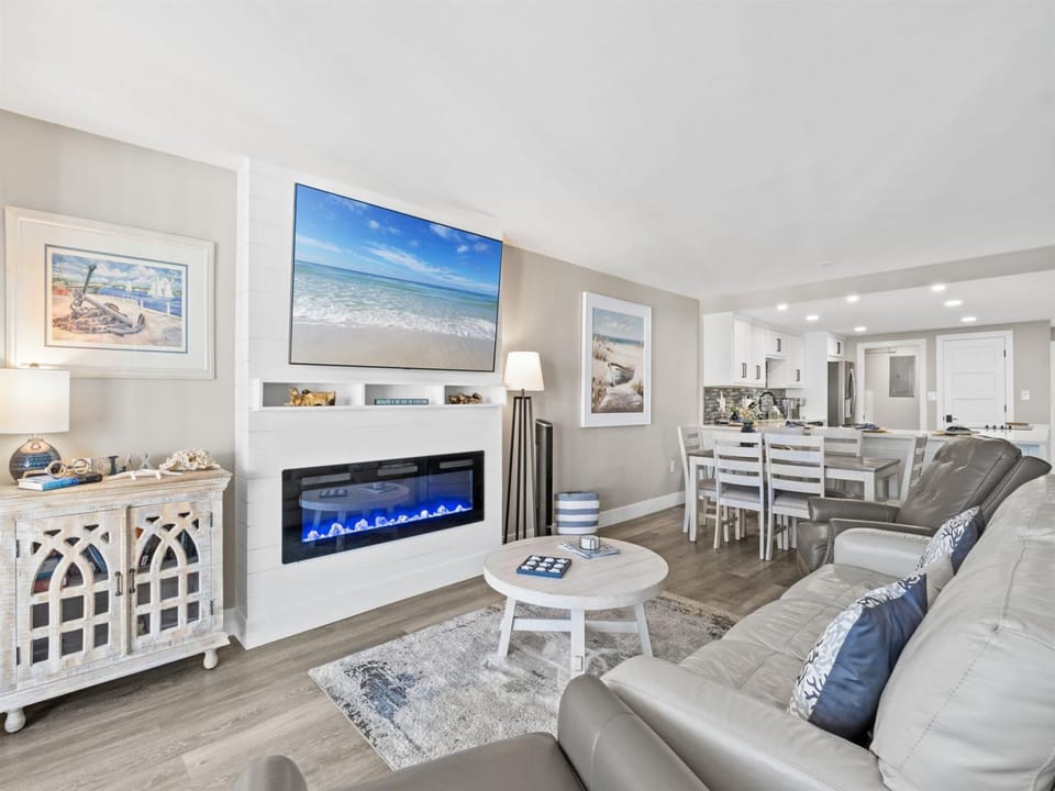 Relax in your sophisticated living area with coastal artwork, electric fireplace, and open kitchen perfect for memorable evenings together.