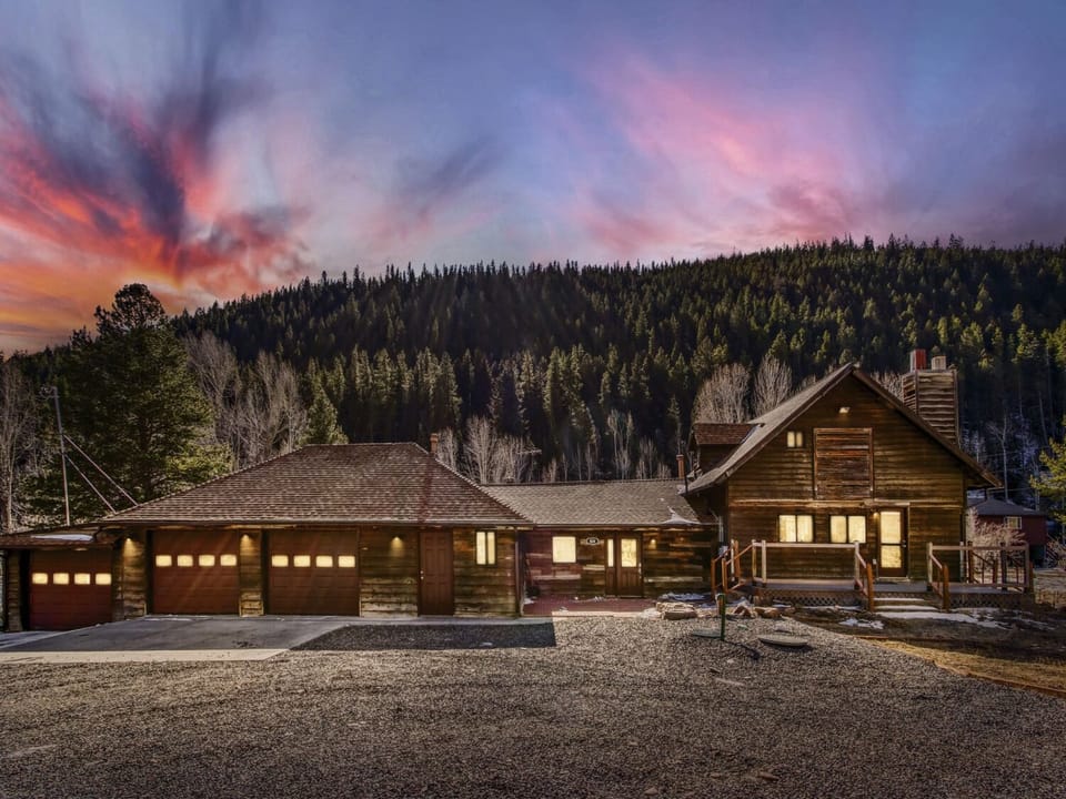 Mountain lodge nestled against forested hillside with dramatic sunset creating spectacular backdrop for this rustic retreat.