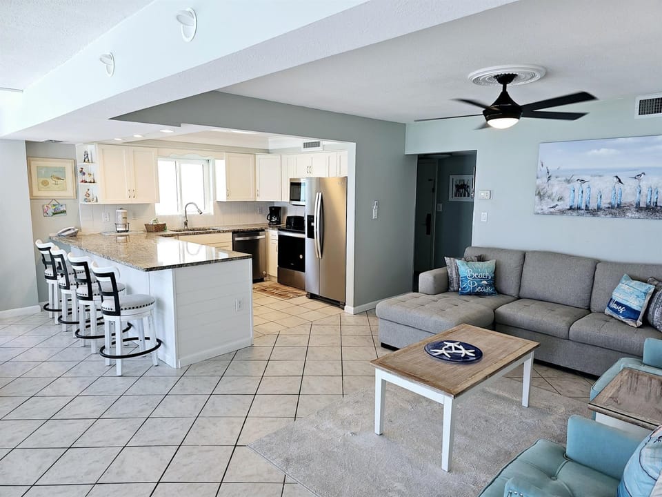 Relax in your spacious open-plan living space with fully-equipped kitchen, comfortable seating, and coastal-themed décor for the perfect beach getaway.