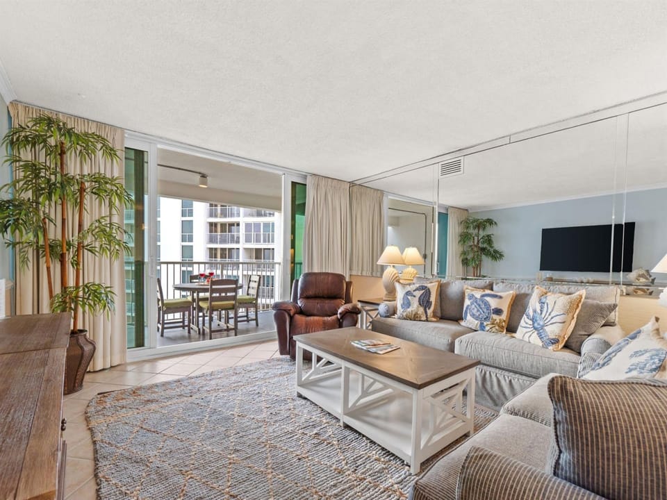 Sink into your spacious living room with plush seating, coastal decor, and balcony views that invite you to relax and unwind.