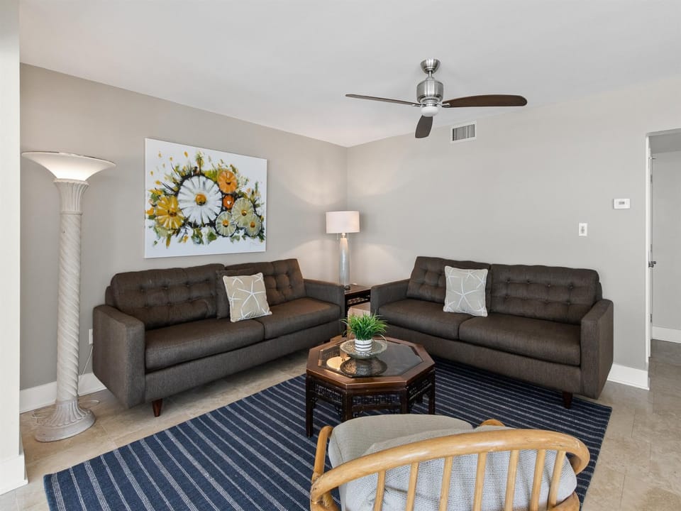 Relax in your spacious living room featuring plush seating, cheerful artwork, and gentle ceiling fan comfort for perfect temperature control.