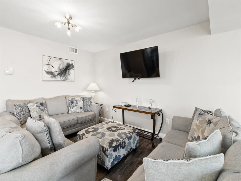 Relax in your spacious living room with plush gray seating, modern entertainment center, and elegant décor creating the perfect retreat.