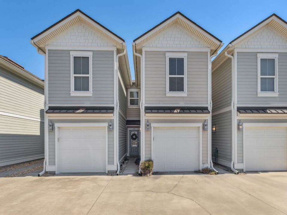 Modern townhome exterior with private garage and charming architectural details under clear blue skies.