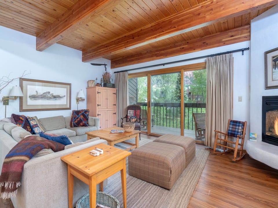 Unwind in your cozy living space with vaulted wood ceilings, a crackling fireplace, and doors opening to your private balcony overlooking lush greenery—perfect for peaceful mornings and relaxing evenings.