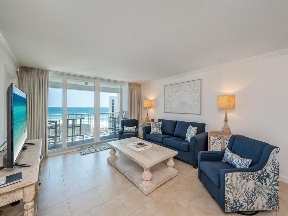 Relax in your spacious oceanfront living room with stunning sea views through floor-to-ceiling windows and comfortable coastal-themed seating.