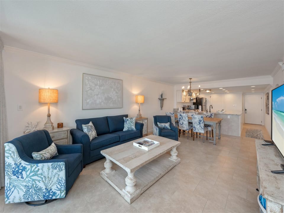 Relax in your elegant living room with plush navy seating, warm coastal lighting, and an open kitchen perfect for entertaining.