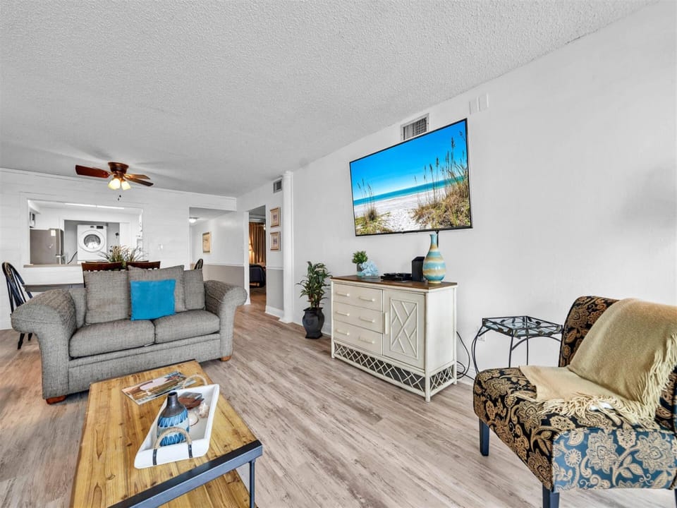 Relax in your bright living space with coastal-themed touches, modern furnishings, and a large TV displaying beautiful beach views.