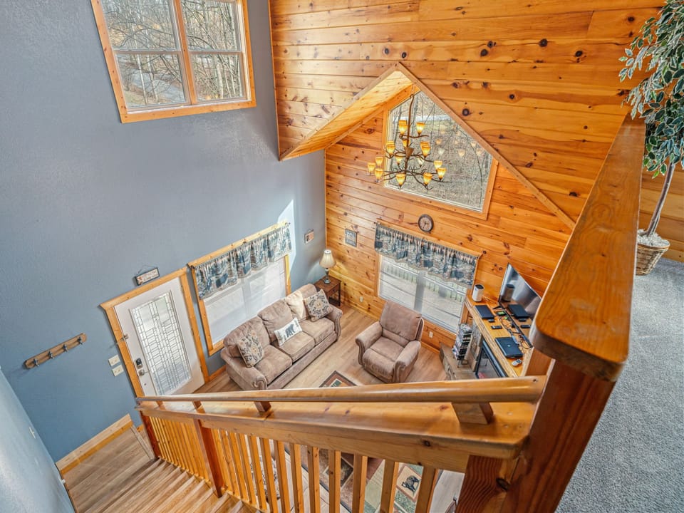 Enjoy sweeping views of your cozy living space from the rustic wooden loft, where natural light pours through expansive windows into the spacious retreat below.