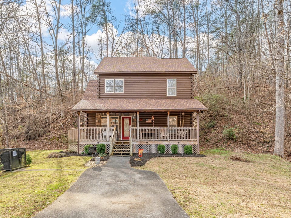 Charming log cabin nestled in a wooded setting with welcoming front porch and peaceful natural surroundings.