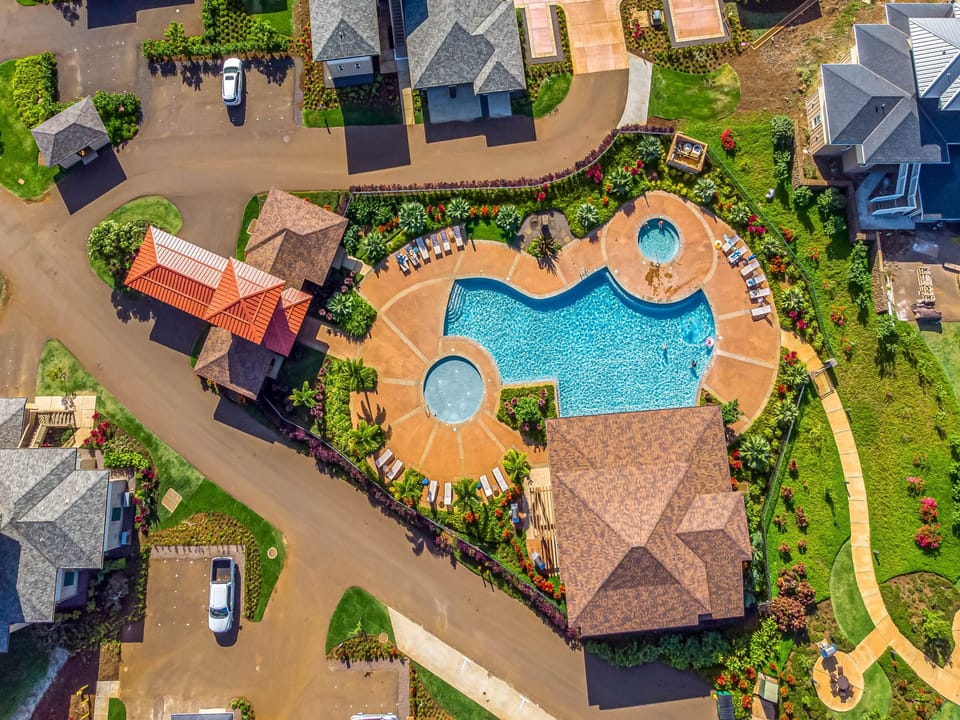 Aerial view showcasing the resort's stunning curved pool complex with hot tub, surrounded by tropical landscaping and residential buildings.