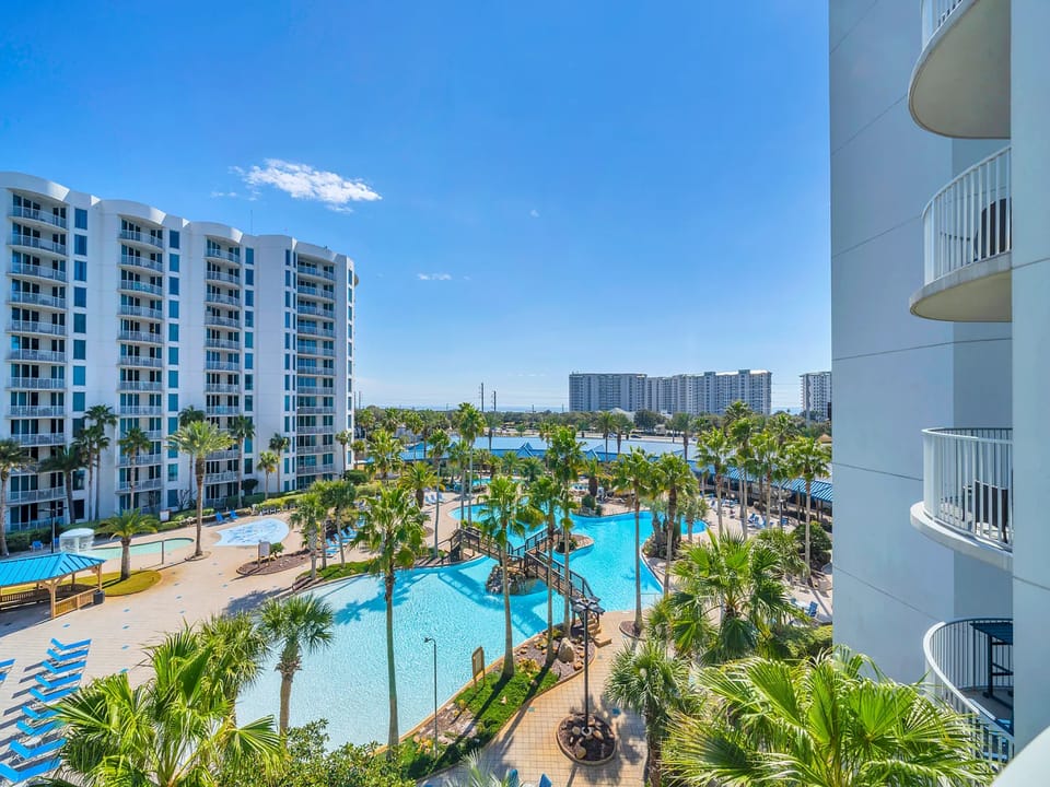 Expansive resort complex featuring multiple swimming pools, waterfront views, and modern high-rise buildings under clear blue skies.