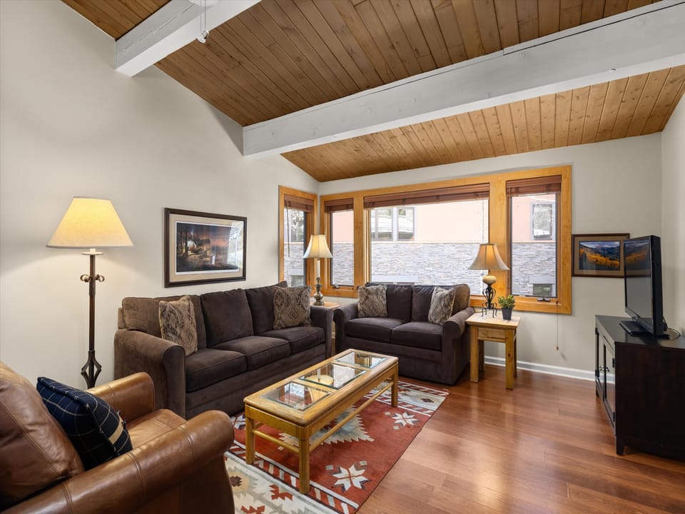 Relax in your spacious living room with vaulted wood ceilings, plush seating, and warm lighting creating the perfect mountain retreat atmosphere.
