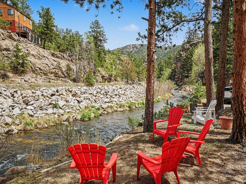A peaceful riverside retreat with towering pines and mountain views framing your private seating area, perfect for unwinding to the sound of flowing water.