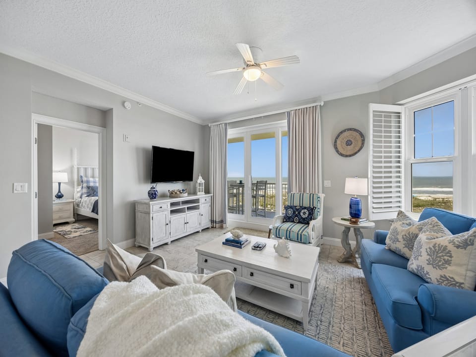 Picture yourself unwinding in this coastal retreat, where soft blue accents and a ceiling fan keep you comfortable as you gaze out at stunning ocean views through sliding doors.