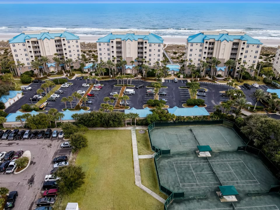 Beachfront resort complex featuring tennis courts, swimming pools, parking, and tropical landscaping along a pristine stretch of coastline surrounded by lush natural vegetation.