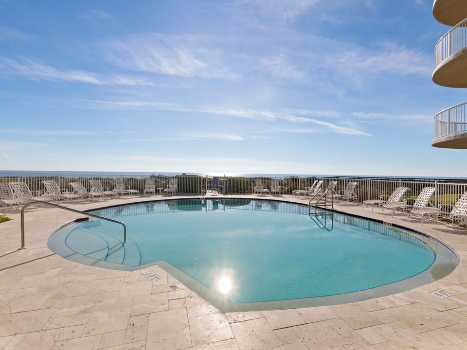 Dive into clear turquoise waters surrounded by plenty of lounge chairs, with peaceful ocean views stretching to the horizon—your sunny escape awaits.