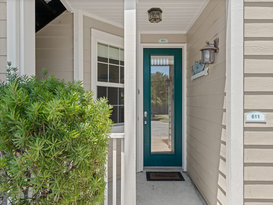A welcoming entrance with a charming teal door, decorative lighting, and tropical greenery marks your arrival to unit 611, setting the tone for your coastal escape.