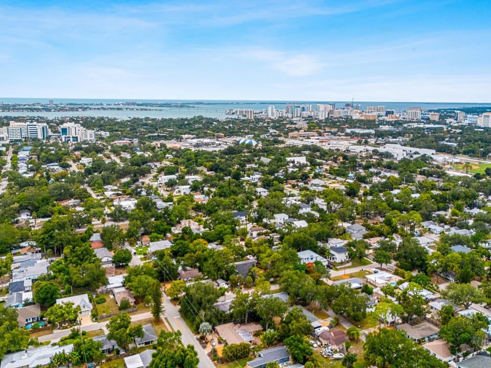 Aerial perspective showing the property's location within a tree-lined residential neighborhood, with bay and city skyline visible in the distance.