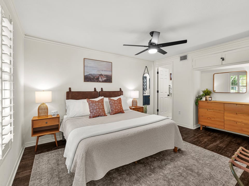 Unwind in your peaceful retreat, featuring a plush bed with stylish linens, warm wood furnishings, soft lighting, and a ceiling fan to keep you comfortable year-round.