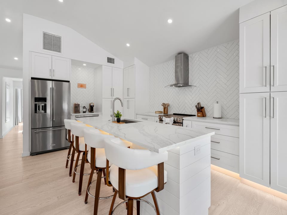 Sleek modern kitchen with marble island, stainless steel appliances, and elegant herringbone backsplash—your culinary haven awaits for meals and memories.