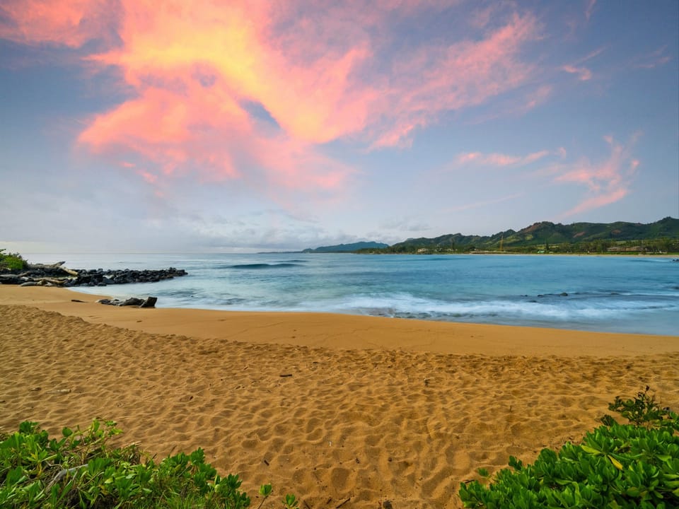 A stunning coastal sunset paints the sky in vibrant pink and orange hues over tranquil turquoise waters.