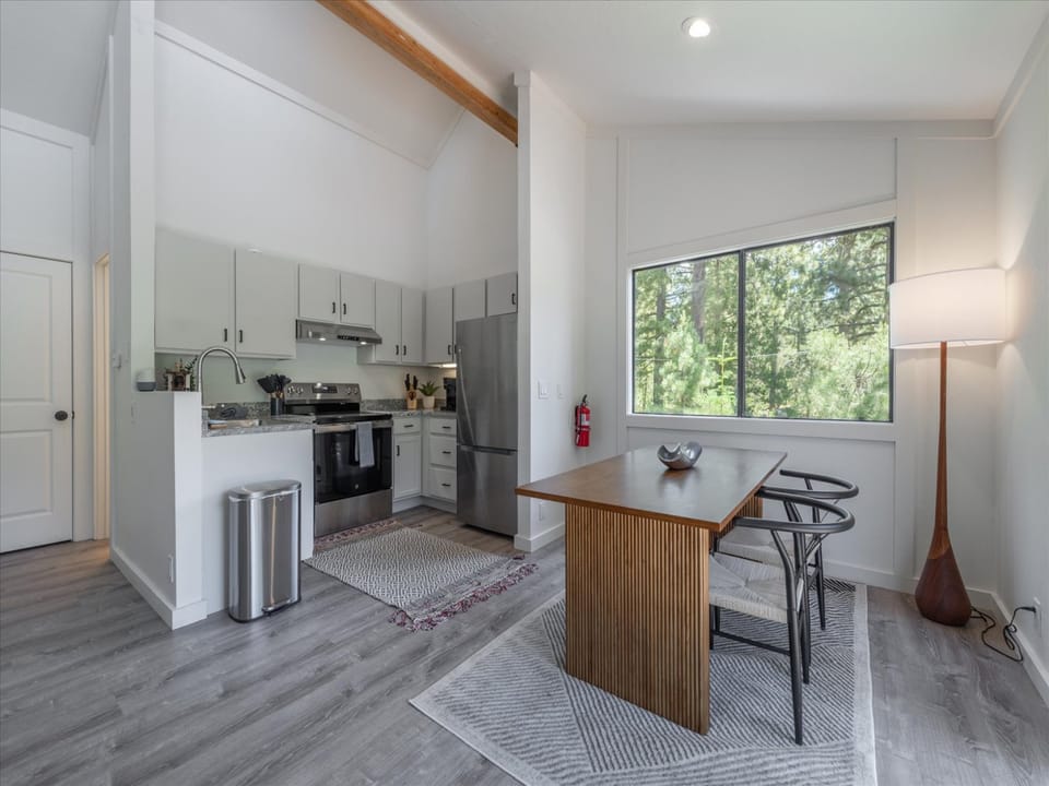 Your bright, modern kitchen features sleek appliances, warm wood accents, and abundant natural light—perfect for preparing meals while enjoying peaceful tree-lined views through the large window.