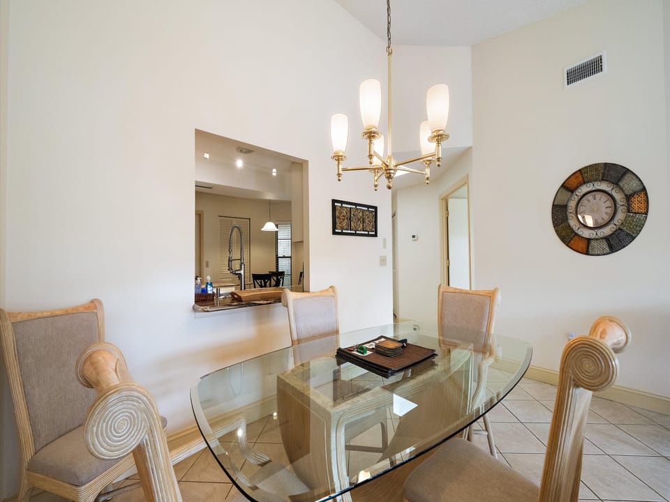 Gather around the elegant glass dining table, where warm light from the classic chandelier sets the perfect mood for your meals together. The open kitchen beyond invites easy conversation and connection.