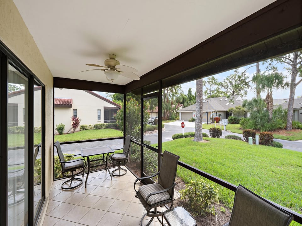 A screened patio overlooks a residential neighborhood with green lawns and palm trees, offering a peaceful setting for outdoor relaxation near the property entrance.
